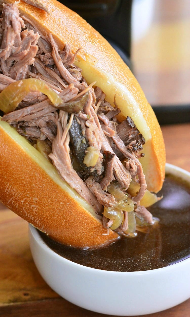 side view of Mushroom and Onion Italian Beef sub being dipped in au jus sauce 