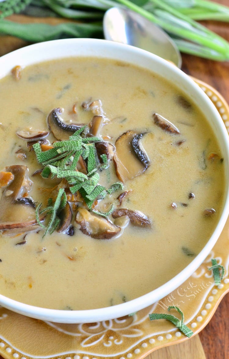 top view of Mushroom soup in white bowl on light brown plate and spoon next to it