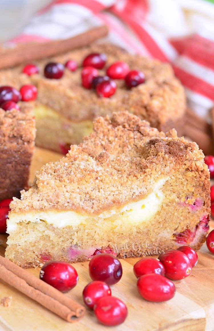 A slice of Cranberry Cream Cheese Coffee Cake on a cutting board with the rest of the cake in the background 