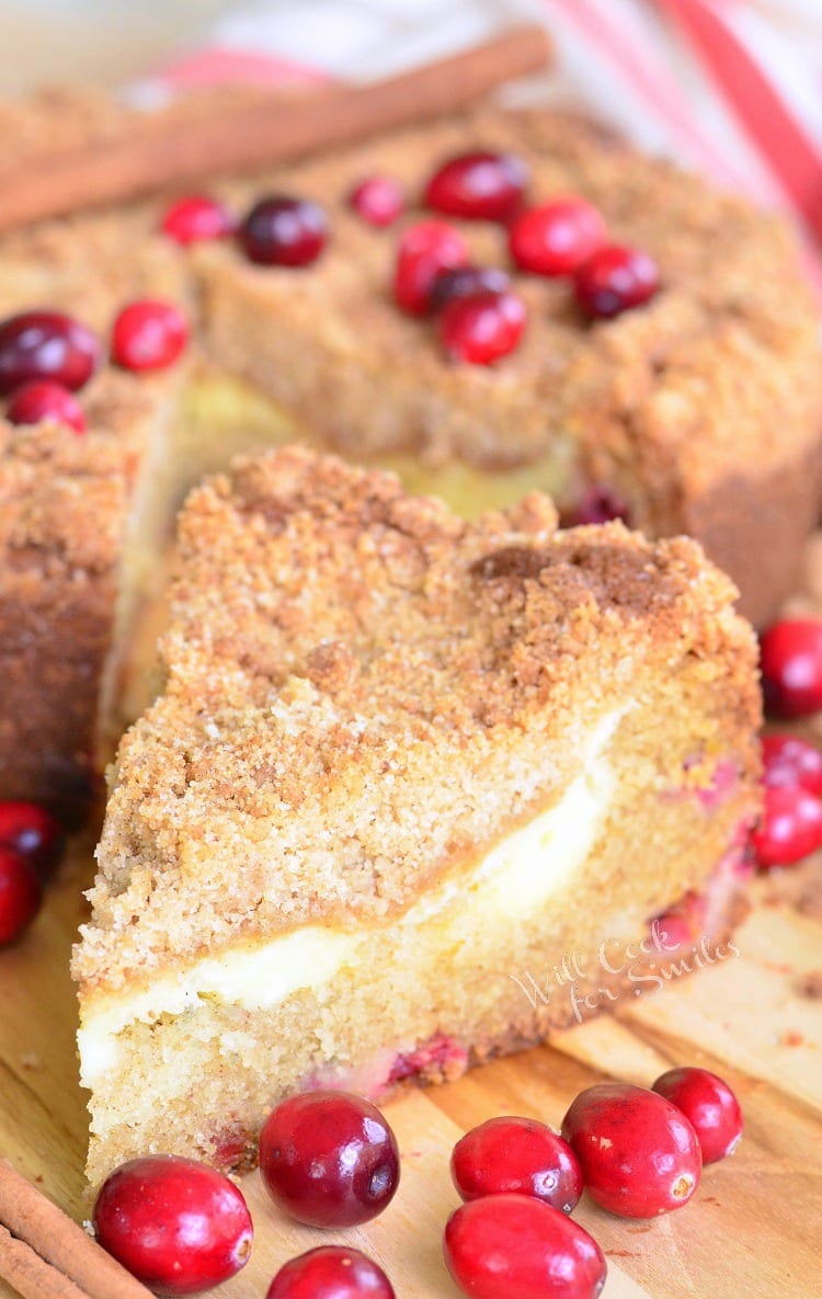 A slice of Cranberry Cream Cheese Coffee Cake on a cutting board with the rest of the cake in the background 