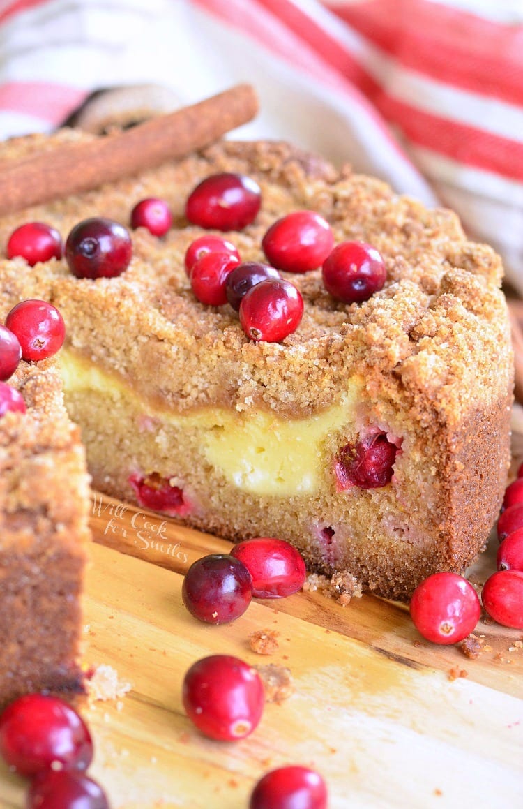 Cranberry Cream Cheese Coffee Cake on a cutting board with a slice missing and cranberries all around it 