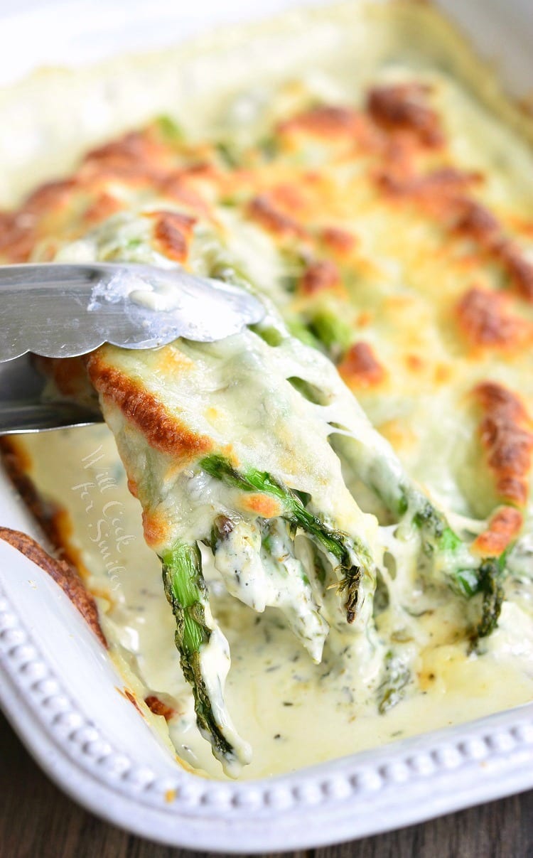 Creamy Italian Asparagus being lifted out of a white serving dish with tongs 