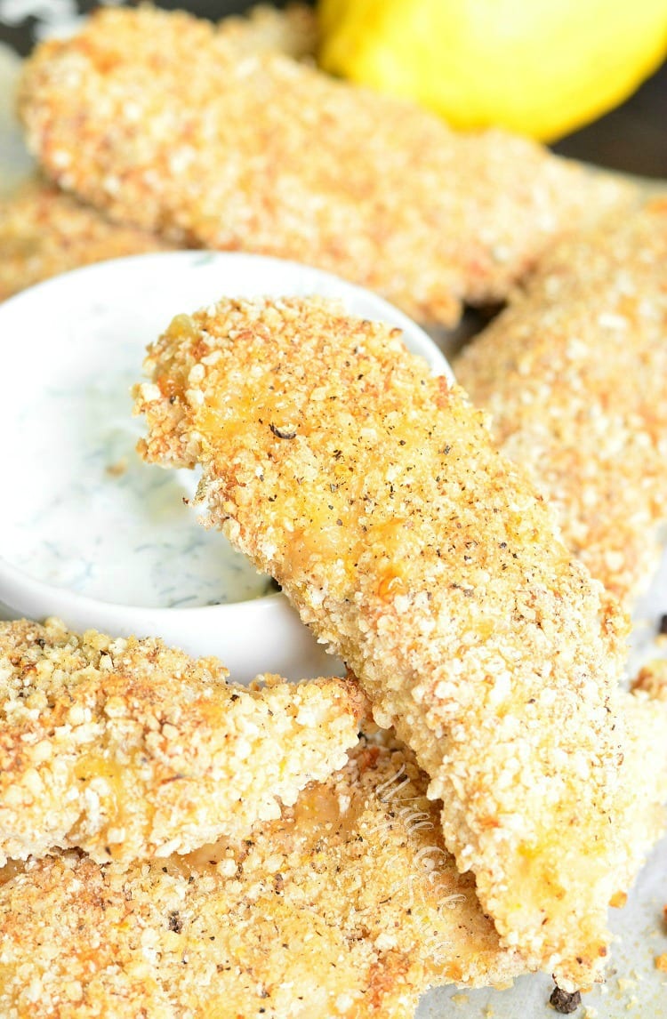 Lemon Pepper Baked Chicken Tenders stacked on a plate with dipping sauce in a white bowl 