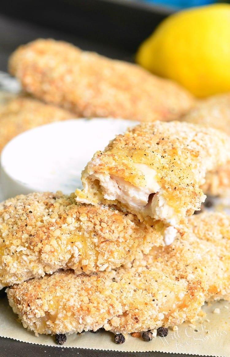 Lemon Pepper Baked Chicken Tenders stacked on wax paper with dipping sauce in a white bowl in the background 