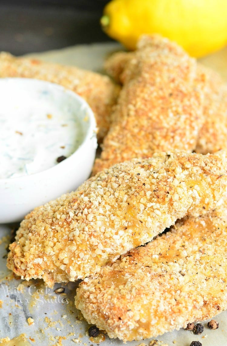 lemon pepper baked chicken tenders on a piece of wax paper with a white bowl of dipping sauce 