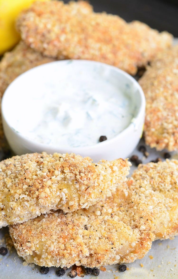 Lemon Pepper Baked Chicken Tenders on a baking dish with dipping sauce in a white bowl 