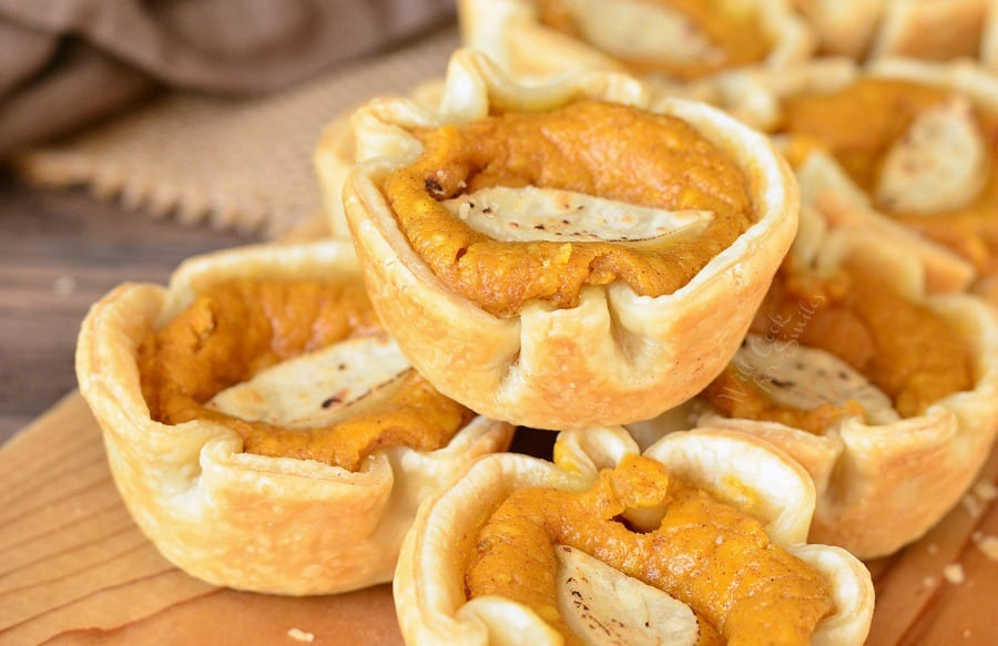 several mini pumpkin cheesecake pies stacked on a wooden table.