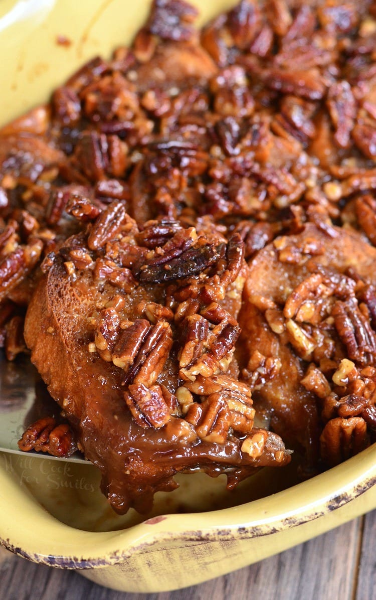 lifting Pecan Pie French Toast Casserole out of a yellow casserole dish with a spatula 