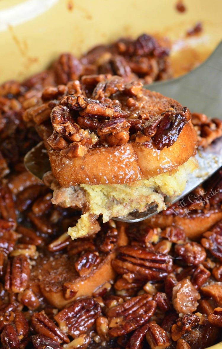 Pecan Pie French Toast Casserole in a yellow casserole dish lifting a piece out with a spatula 