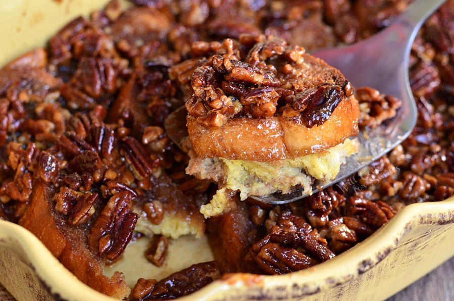 Pecan Pie French Toast Casserole in a yellow casserole dish being lifted out with a spatula 