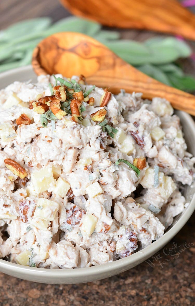 Pecan, Sage, and Gruyere Turkey Salad in a white bowl with a wood spoon above the bowl 