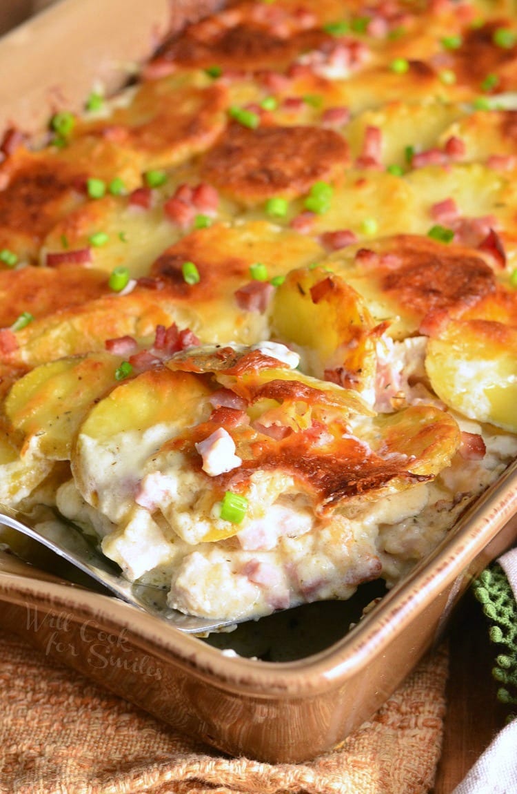 Chicken Cordon Bleu Scalloped Potatoes in a brown casserole dish with a spatula lifting a piece out 