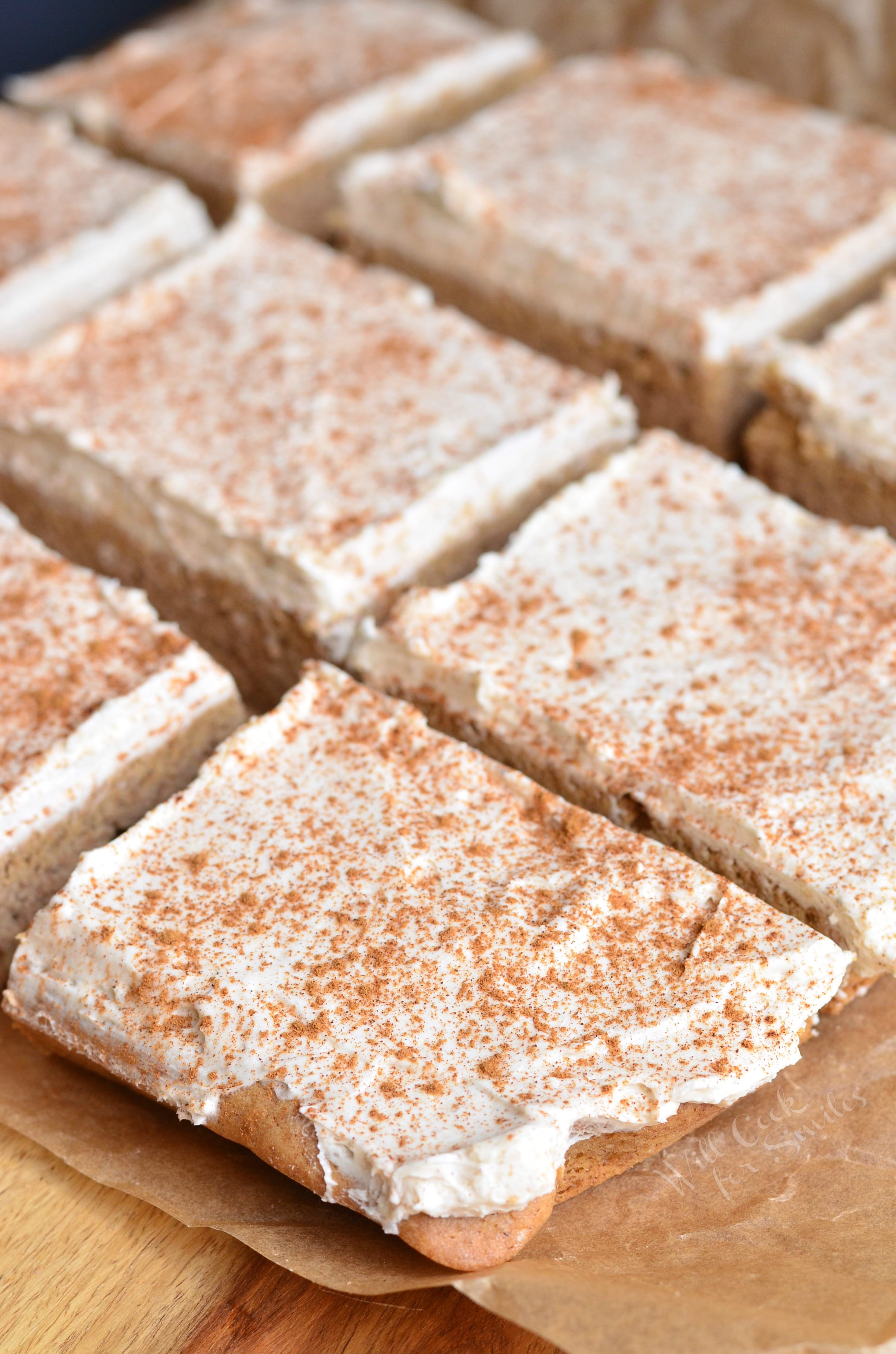 Cinnamon Brown Butter Sugar Cookie Bars with frosting on top on a piece of wax paper on a wood cutting board 