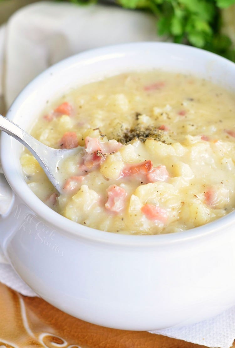 spooning some cauliflower soup with metal soup spoon from a white bowl