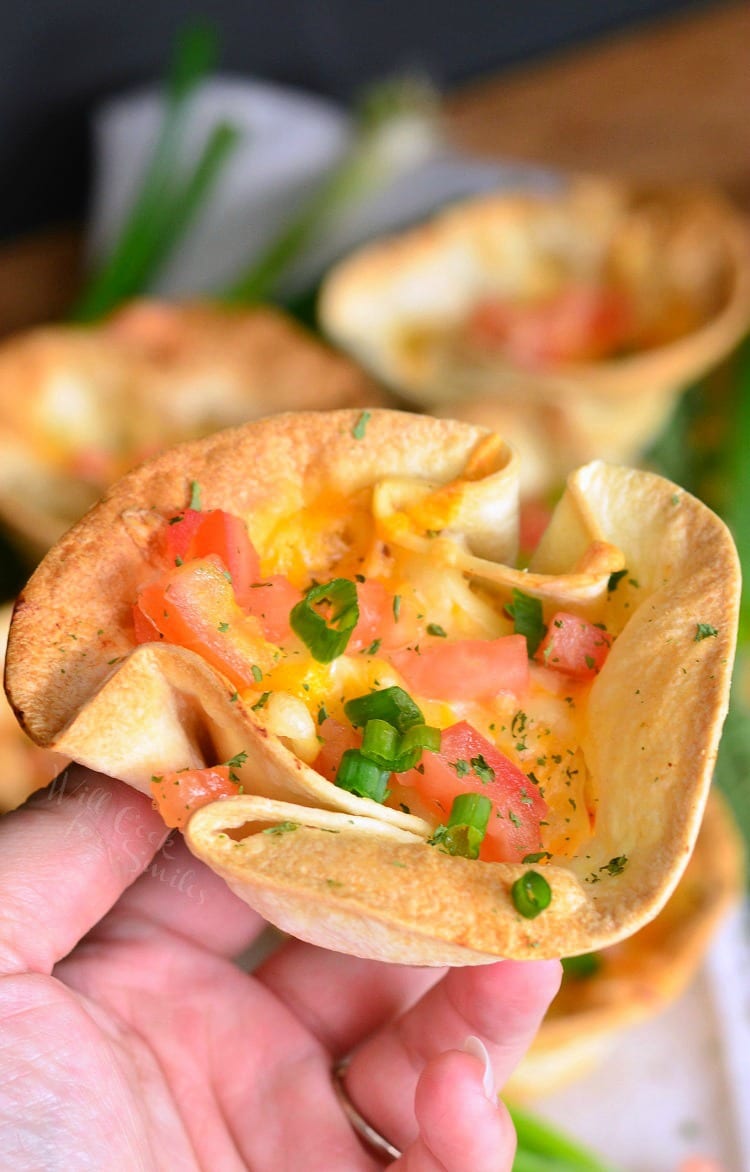 holding an enchilada cup dilled with chicken, tomatoes, and green onions