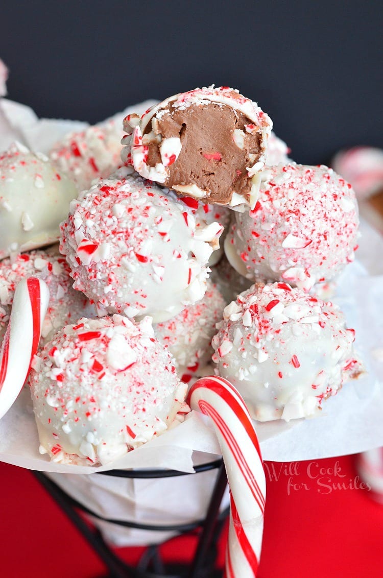 fudge truffles coated in white chocolate and crushed peppermint in a metal bowl with candy canes one truffle on to is cut in half
