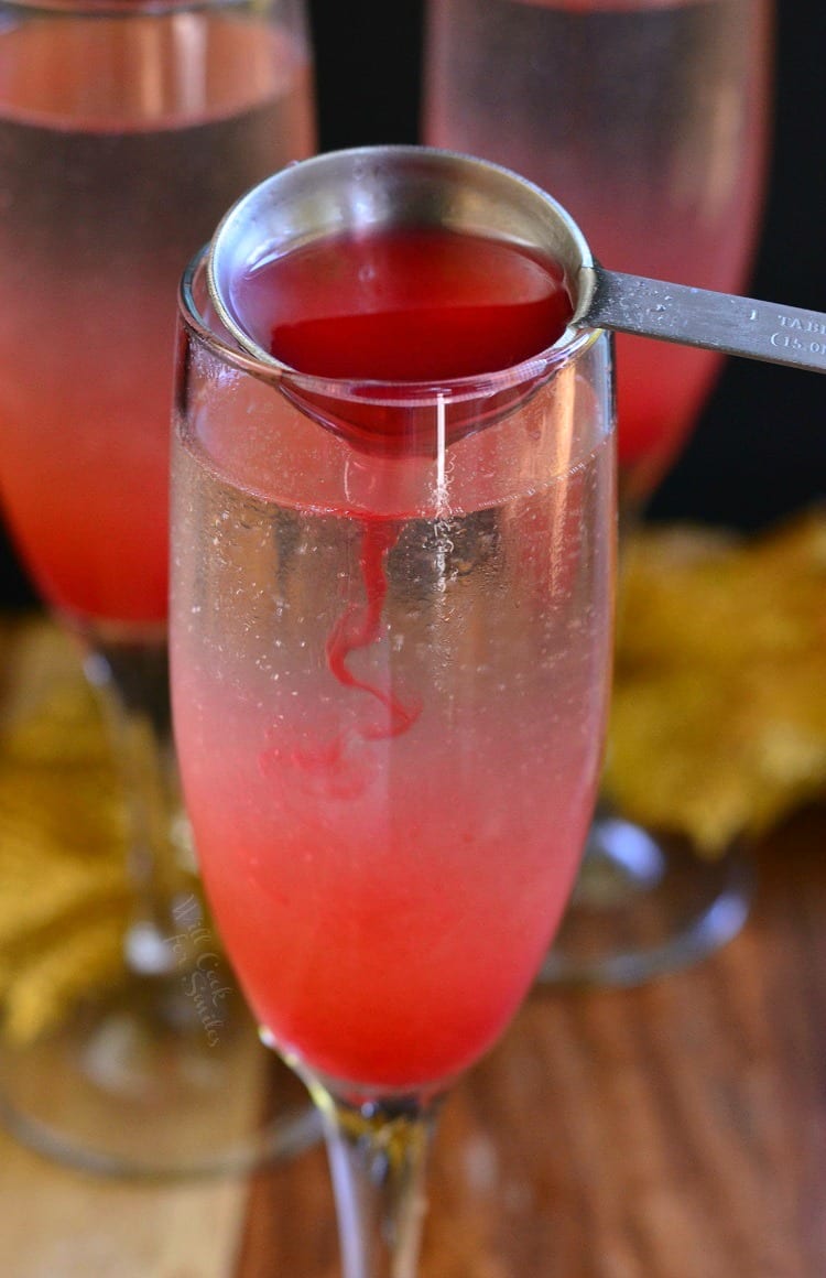 Raspberry Italian Soda Champagne Cocktail in a champagne flute on a table pouring the raspberry into glass with a measuring spoon 