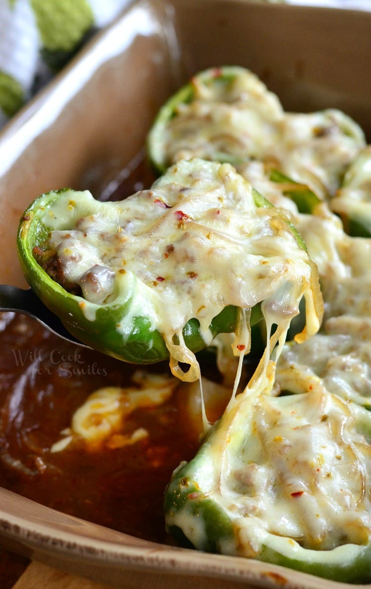 lifting a Salisbury Steak Stuffed Pepper with cheese on top in a brown casserole dish out of pan with a serving spoon 