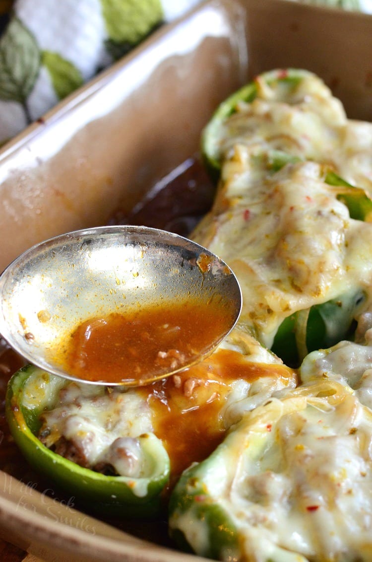 pouring sauce over the Salisbury Steak Stuffed Peppers that are in a brown casserole dish 