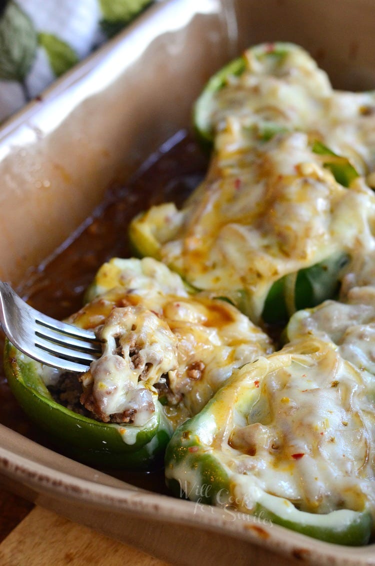 Salisbury Steak Stuffed Peppers with cheese on top in a brown casserole dish with a fork going into them 