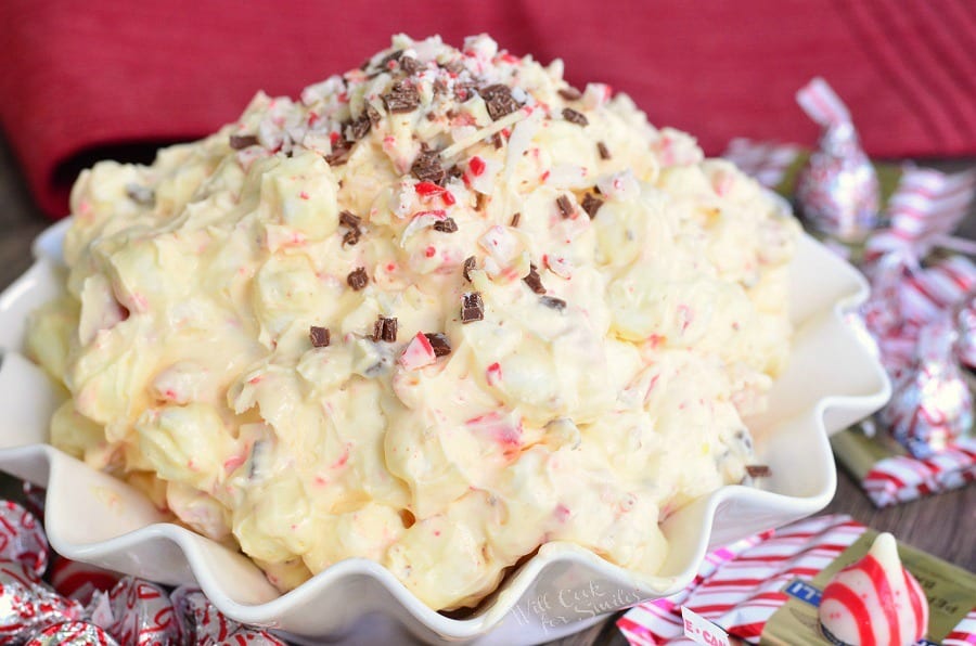 White Chocolate Peppermint Fluff Salad in a white bowl with peppermint kisses around it 