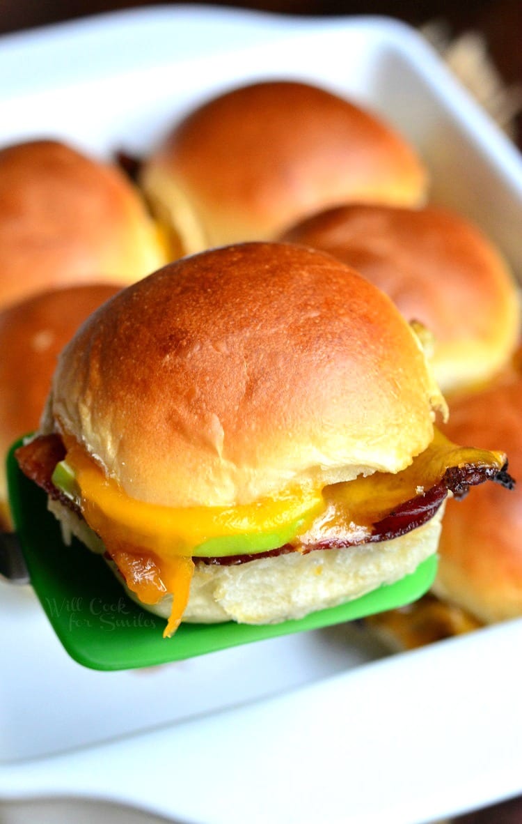 Apple Bacon Cheddar Slider being lift out with a green spatula of a white baking dish