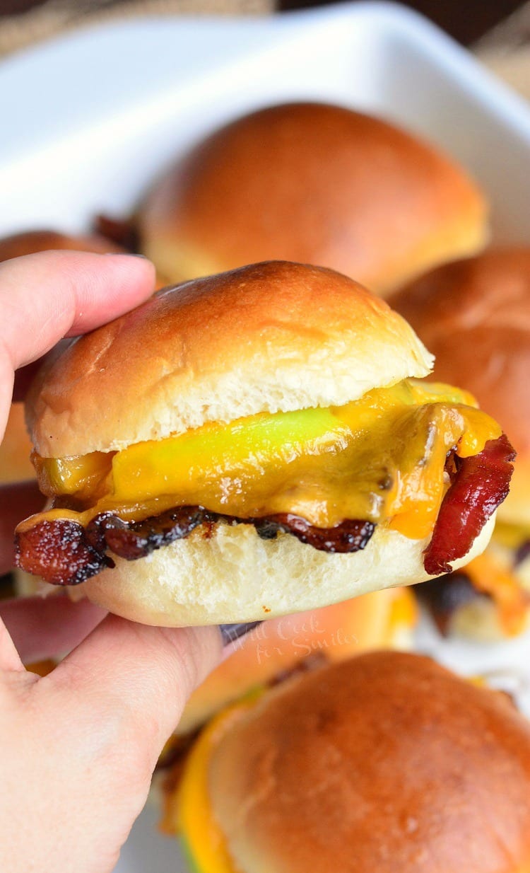 holding a Apple Bacon Cheddar Baked Slider with the rest in the background in a baking dish 