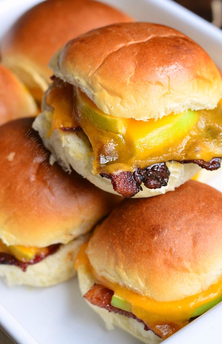 Apple Bacon Cheddar Baked Sliders stacked on top of each other in a white baking dish 