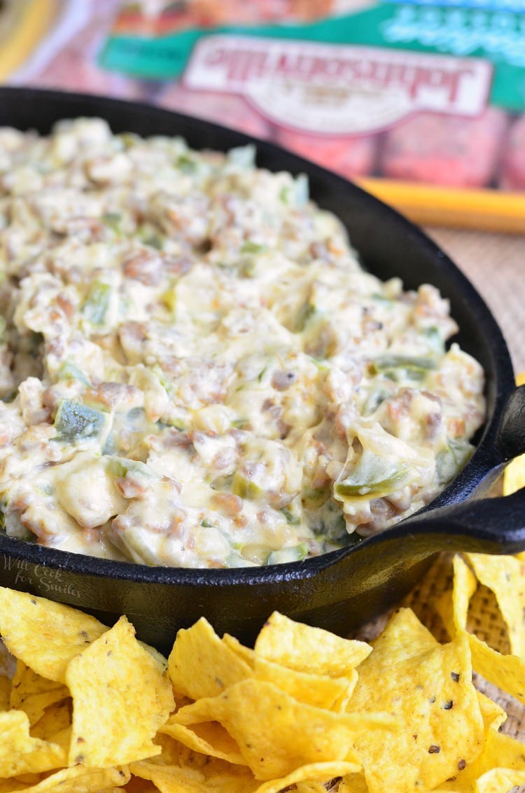 Cheesy Sausage Peppers and Onions Dip in a cast iron pan with chips around it 