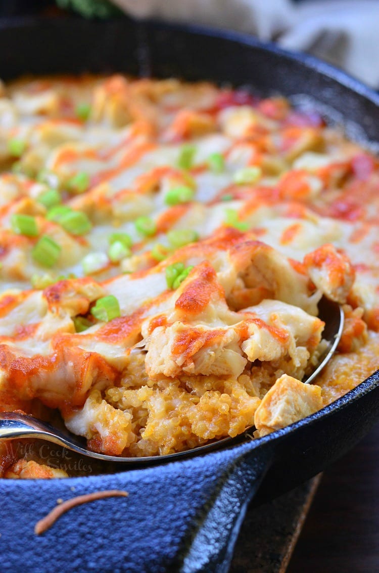 Creamy Sriracha Chicken and Quinoa Bake in a cast iron skillet with a spoon lifting some out 