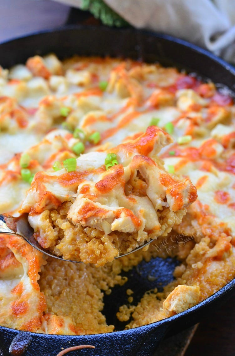 Creamy Sriracha Chicken and Quinoa Bake in a cast iron skillet with a spoon lifting some out 