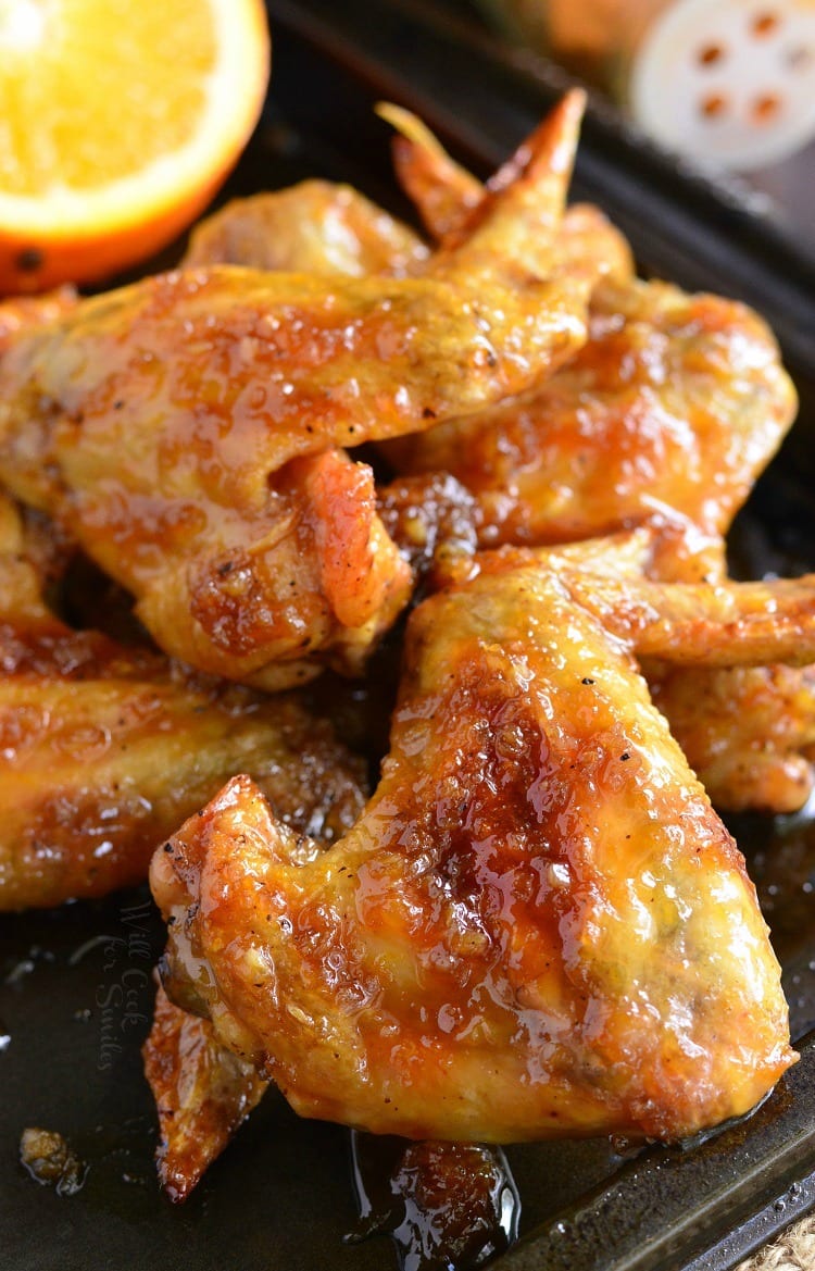 Spicy Orange Chicken Wings stacked on a cooking sheet on the top right corner is a slice of orange 