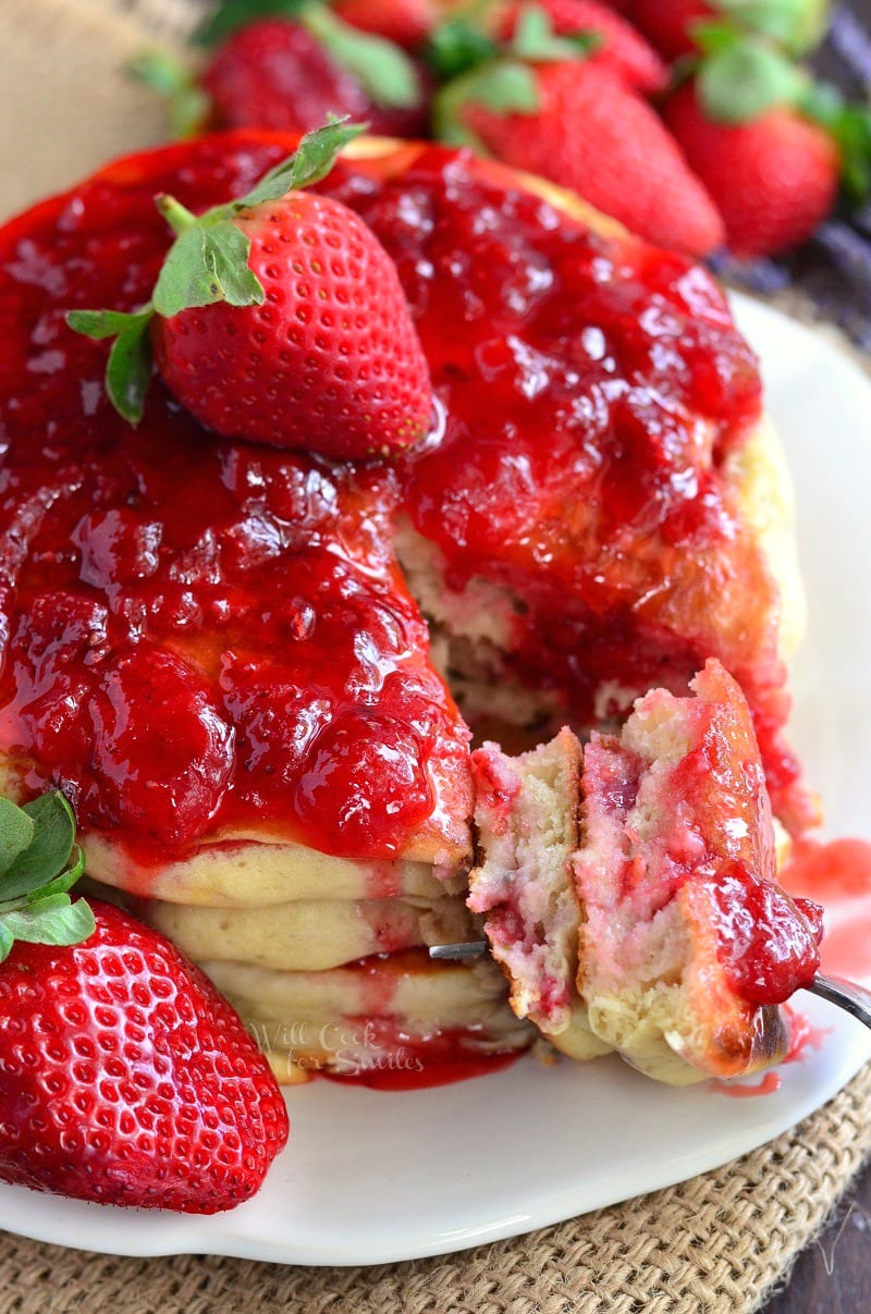 strawberry pancakes with strawberry sauce and whole strawberries on top.