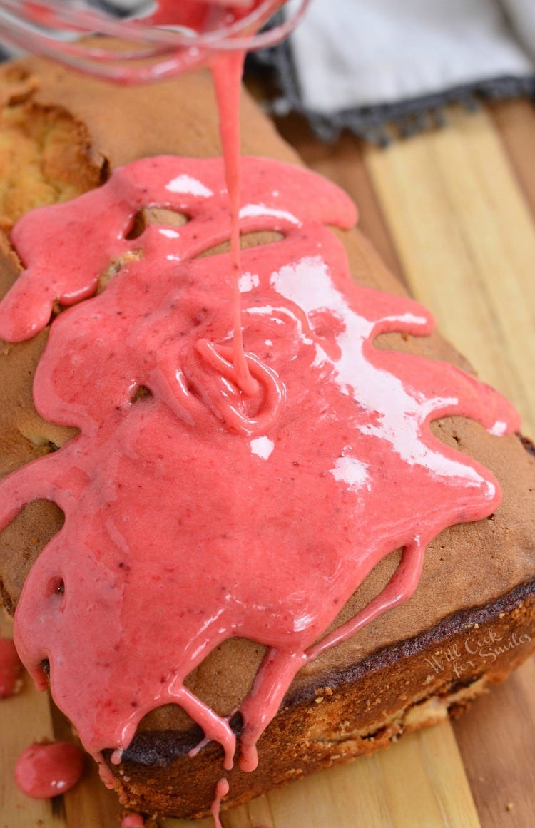 pouring strawberry glaze over pound cake that is on a wood cutting board.