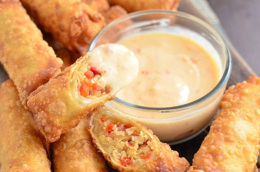 Sweet Chili Chicken Egg Rolls with Creamy Sweet Chili Sauce in a glass bowl with some sauce on on of the rolls 