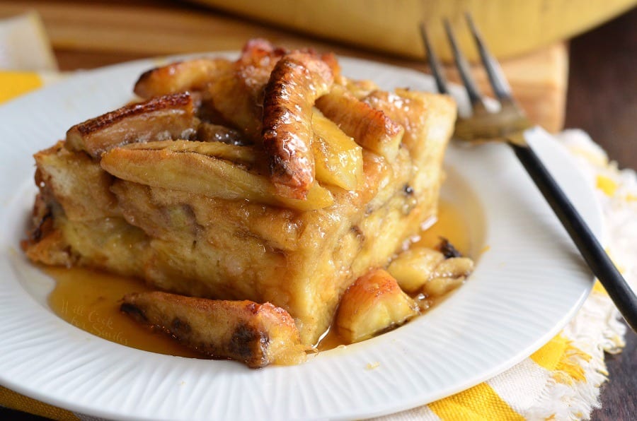 Bananas Foster Bread Pudding on a glass plate with a fork on a plate to the right 