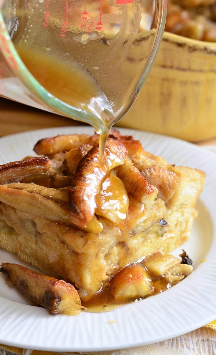 pouring syrup out of a measuring cup over Bananas Foster Bread Pudding that is on a white plate 