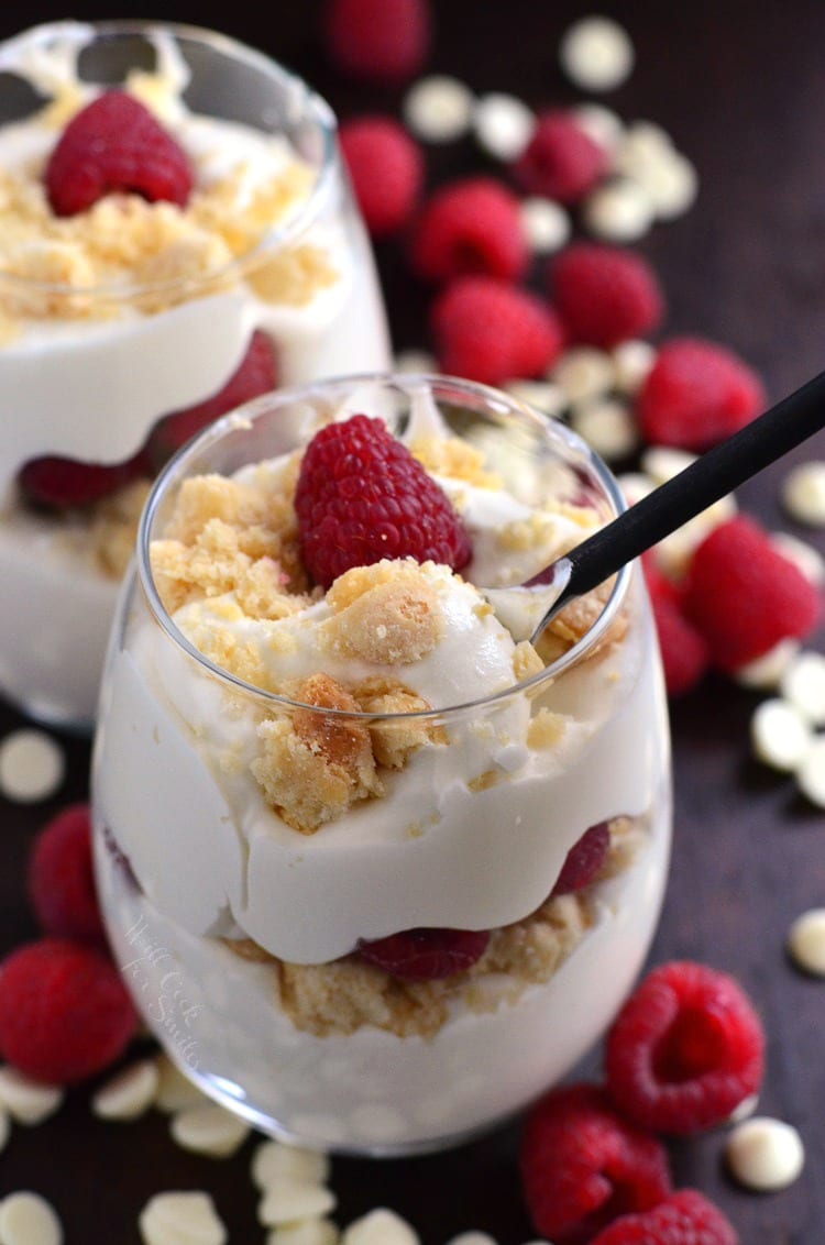 Raspberry White Chocolate Mousse Parfait in a stemless wine glass on a table with white chocolate chips and raspberries 