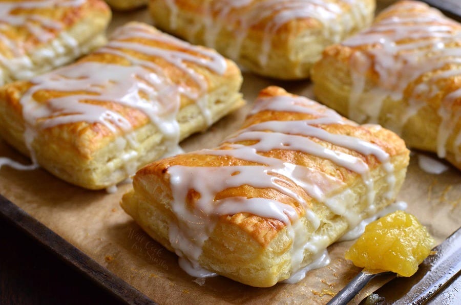 Lemon Cheesecake Hand Pies on a baking dish lined with butcher paper with a spoon full of lemon curd 