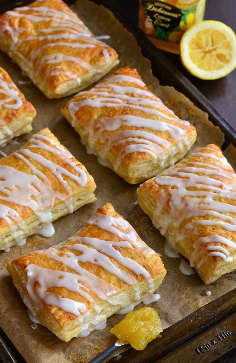 top view of Lemon Cheesecake Hand Pies on a baking sheet lined with butcher paper with a spoon full of lemon curd 