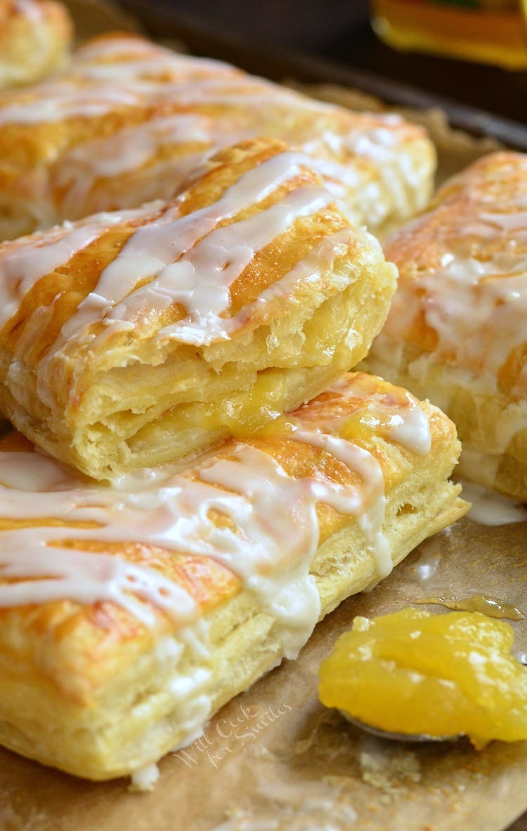 Lemon Cheesecake Hand Pies stacked on a baking sheet lined with butcher paper with a spoon to the right of lemon curd 