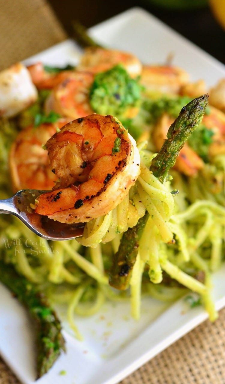 Lemon Pistachio Pesto Pasta with Shrimp and Asparagus on a white plate with a shrimp on a fork 