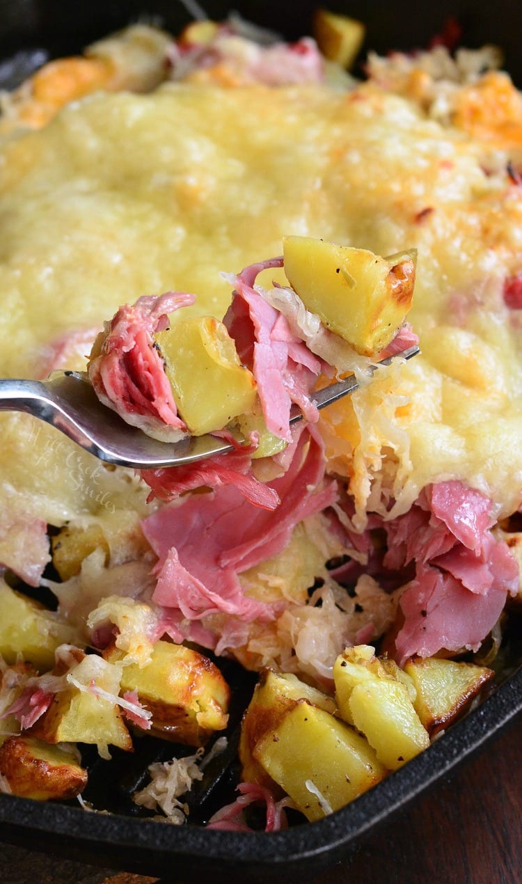 Reuben Loaded Roasted Potatoes with cheese on top in a cast iron skillet with fork scooping some out 