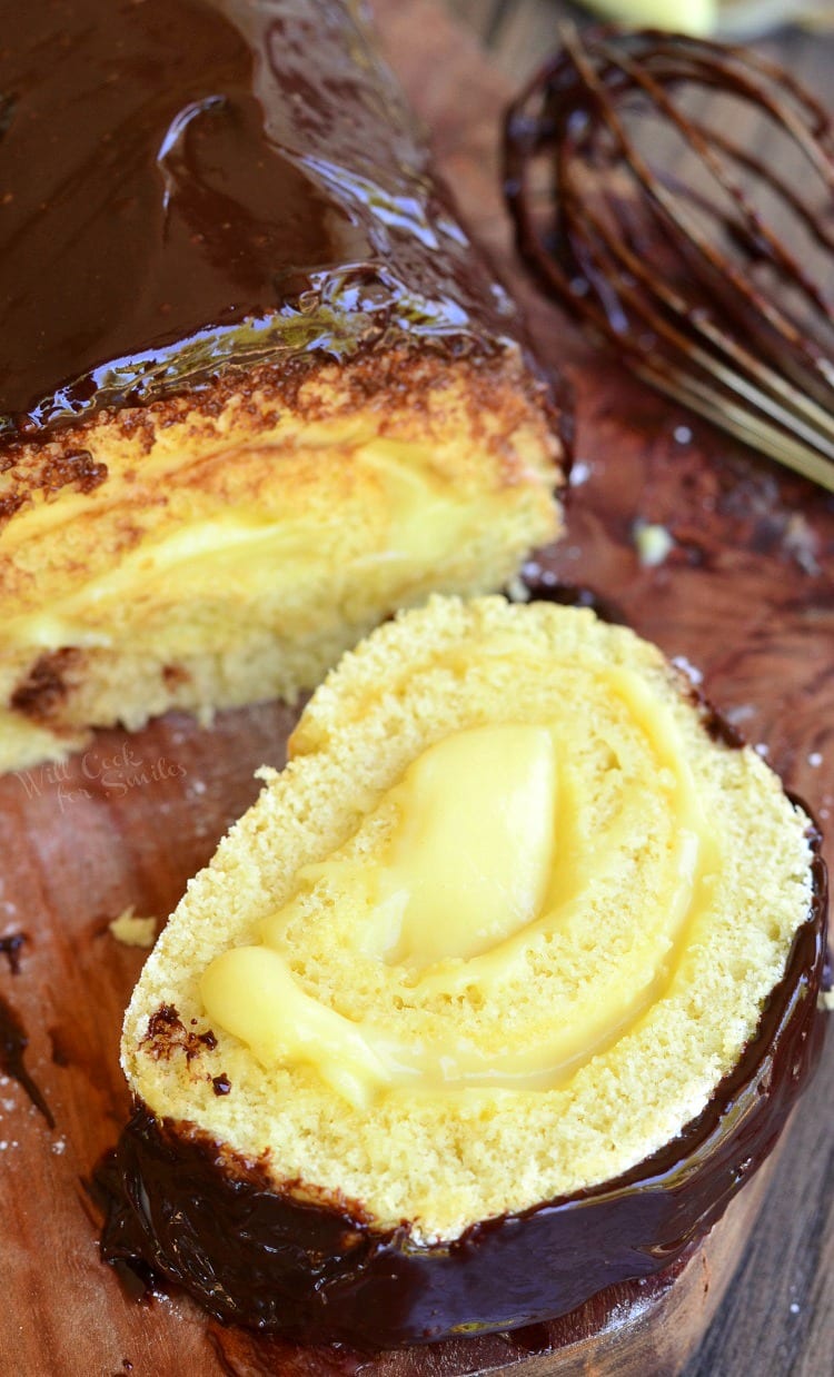 top view Boston Cream Cake Roll with a piece cut off on a cutting board with a whisk in the background 