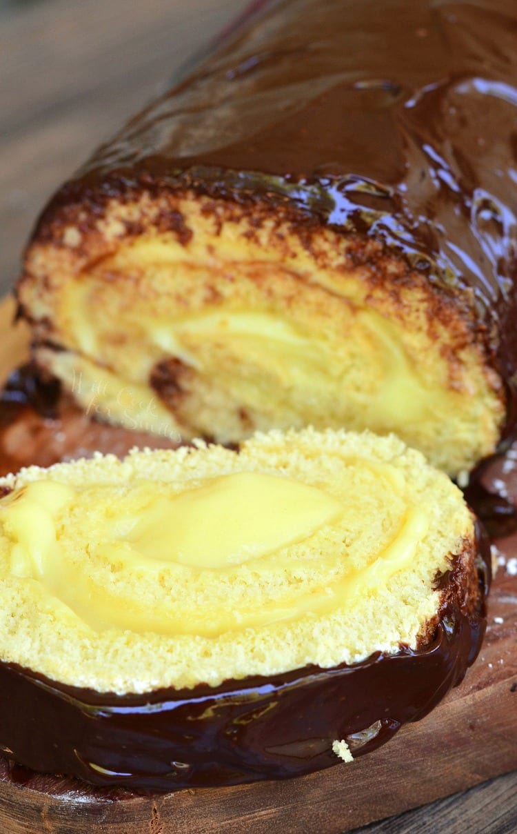 Boston Cream Cake Roll with a slice on a wood cutting board 