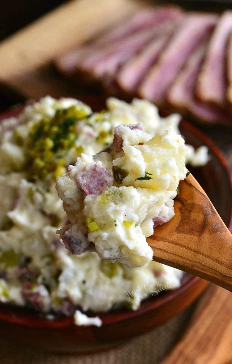 Corned Beef Potato Salad on a wooden spoon with the rest of the potato salad in a wood bowl in the background