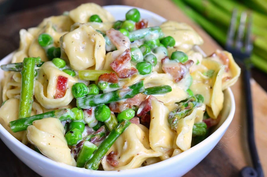 vertical Creamy Spring Tortellini with Peas Asparagus and Bacon in a white bowl on a table with a fork 