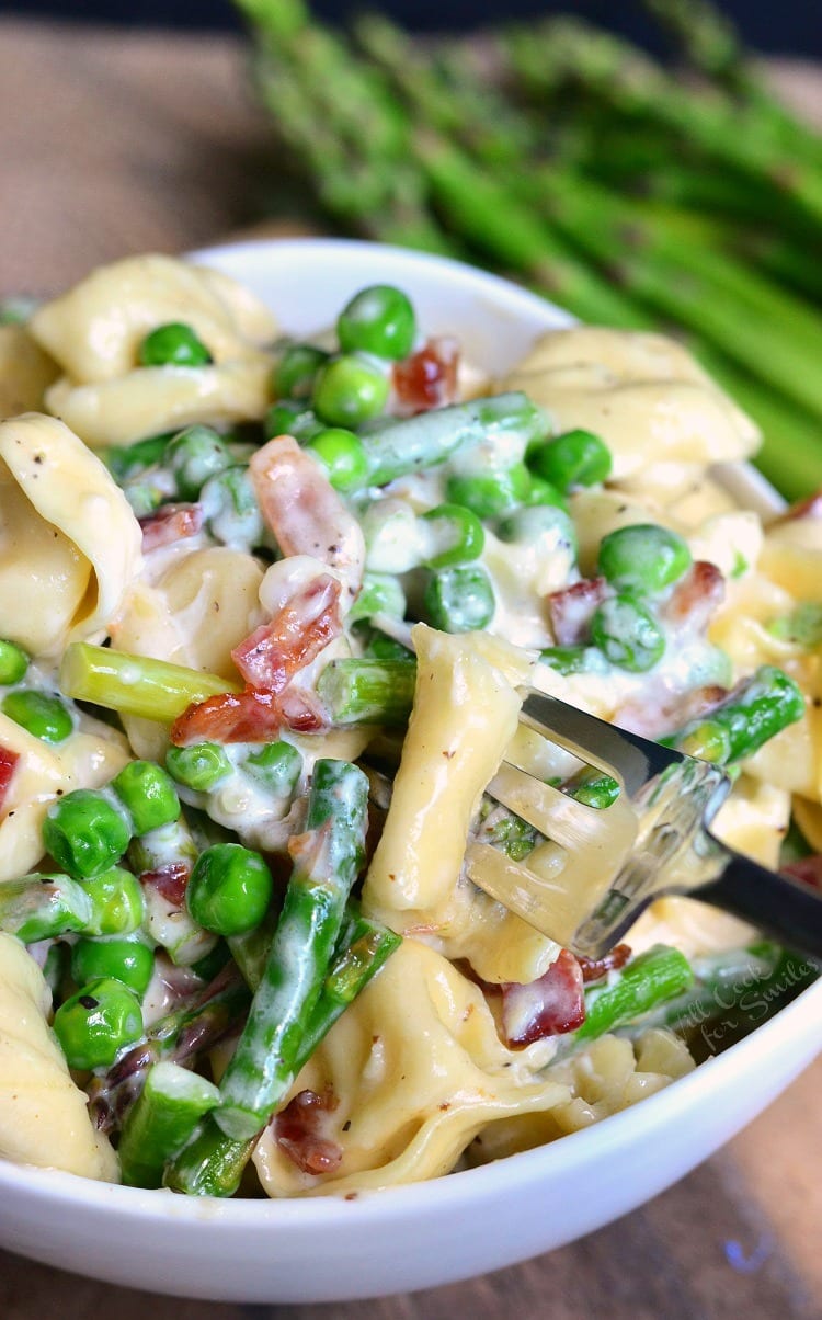 Creamy Spring Tortellini with Peas Asparagus and Bacon in a white bowl with a fork 