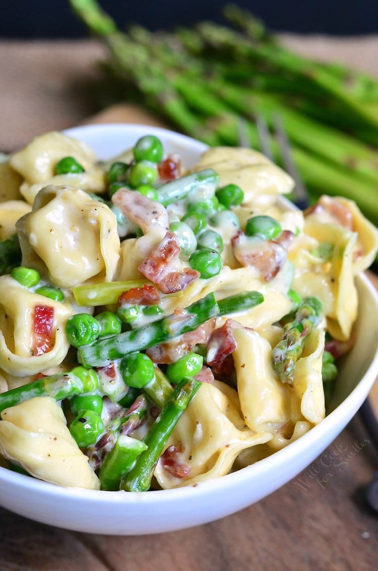 white bowl full of creamy tortellini with vegetables.