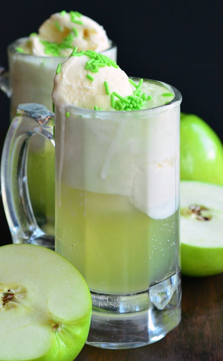 Green Apple Ice Cream Soda Float in a glass mug with green apples around it on a wood table 